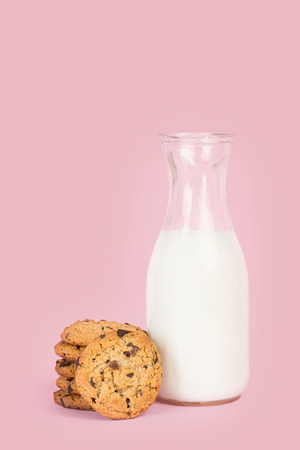 Cookies with chocolate chips and a bottle of milk on a pink backgroundの写真素材