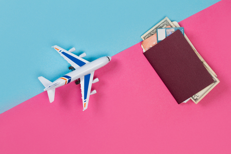 A toy plane with a passport and money on a pink and light blue backgroundの写真素材