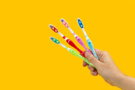 A woman hand holding plastic colored toothbrushes on a yellow backgroundの写真素材