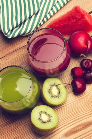 Two half kiwifruit, a plum, cherries and two glass of juiceの写真素材