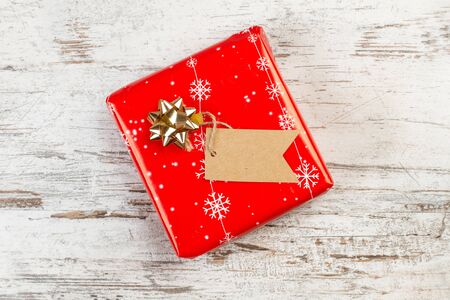 A red christmas gift with a label on a worn out white wooden tableの写真素材