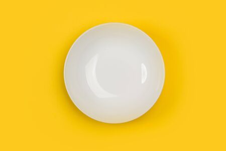 A deep white ceramic plate on a yellow background