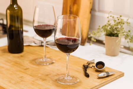 A bottle of red wine and two glasses on a wooden board on the kitchen counter