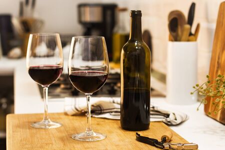 A bottle of red wine and two glasses on a wooden board on the kitchen counterの写真素材