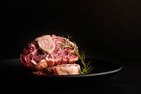 Raw osso buco slices on a black plate