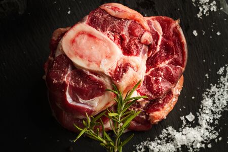 Raw osso buco on a black slab with salt in flakesの写真素材