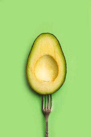 Half avocado with a fork on a green backgroundの写真素材