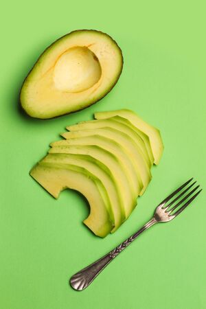 Sliced avocado and a fork on a green backgroundの写真素材