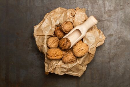 Walnuts in a bowl with a wrinkled paper and a wooden scoop on a rusted metal tableの写真素材