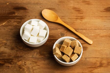 White and brown sugar cubes in white ceramic bowls on a wooden tableの写真素材