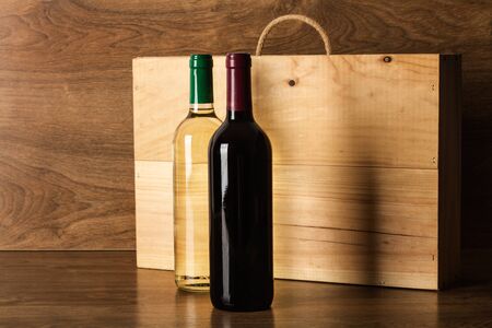 Bottles of red and white wine and a wooden wine box on a wooden tableの写真素材