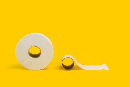 A toilet paper roll and other roll almost empty on a yellow backgroundの写真素材