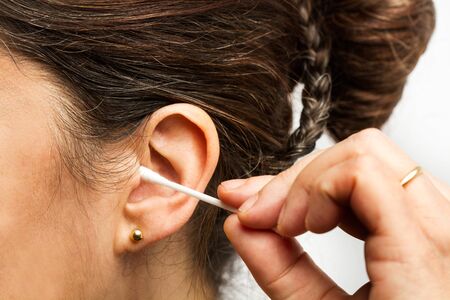 Woman cleaning her ear with a cotton swab in a close up viewの写真素材