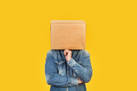 Man with his head in a box and thinking gesture on a yellow backgroundの写真素材