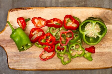 Slices of red, and green peppers on a wooden kitchen board in a top view