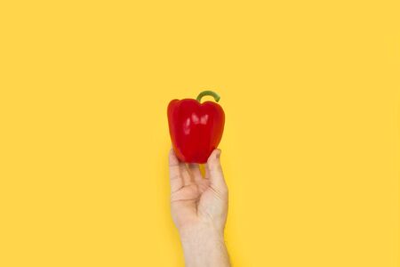 Man hand holding a red bell pepper on a yellow background