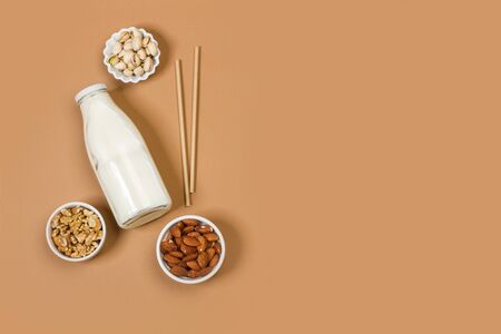 A bottle of milk with nuts in white bowls on a brown background in a top viewの写真素材