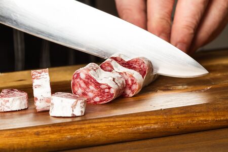 Man cutting a dry pork sausage on a wooden kitchen board