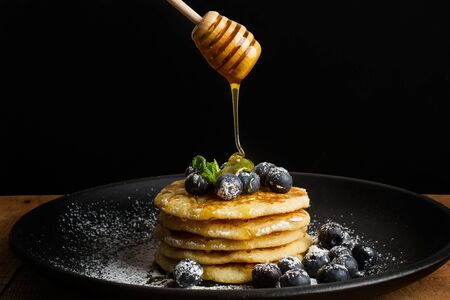 Dipping honey on pancakes with blueberries and icing sugarの写真素材