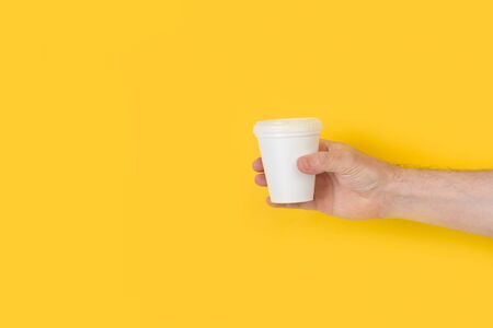 Man´s hand holding a disposable white cup on a yellow backgroundの写真素材