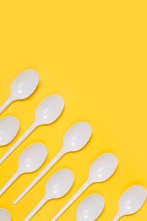 Disposable white plastic spoons on a yellow backgroundの写真素材
