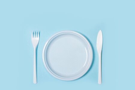 Disposable plastic white cutlery and plate on a light blue background in a top view