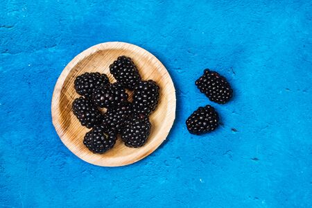 Blackberries on a wooden plate on a textured classic blue background in a top viewの写真素材