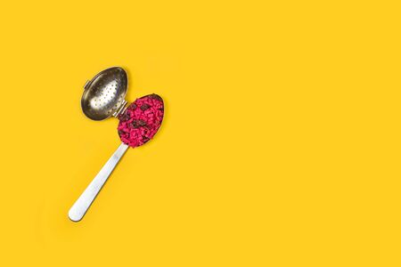 A tea infuser with dry raspberry tea on a yellow background in a top viewの写真素材