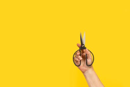Woman hand holding scissors on a yellow background with copy space