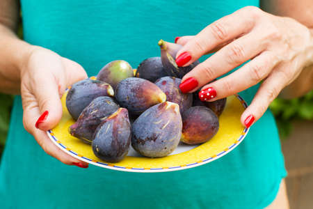 Woman hands with red nails holding a yellow plate with figs