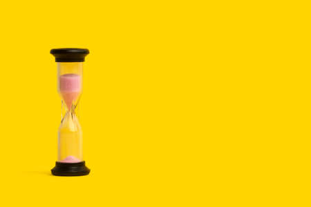 A hourglass with pink sand on a yellow background with copy spaceの写真素材