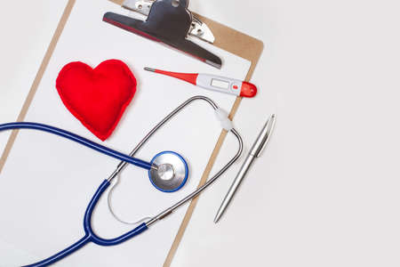 A stethoscope and a thermometer on a clipboard with a fabric red heartの写真素材