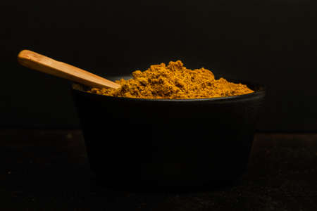 Curry powder in a black bowl on a dark backgroundの写真素材