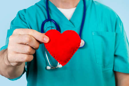 Doctor with a stethoscope holding a red fabric heart in a close up view