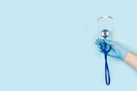 Hand with surgical glove holding a stethoscope on a light blue background with copy space