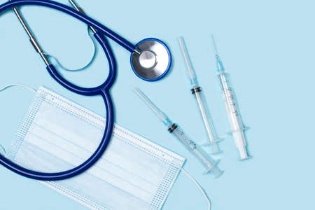 A stethoscope, surgical mask and syringes on light blue backgroundの写真素材