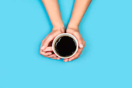 Woman hands holding a cup of black coffee on a light blue background in a top viewの写真素材
