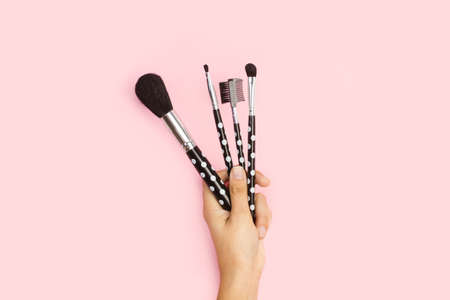 Woman hand holding make up brushes on a pink background