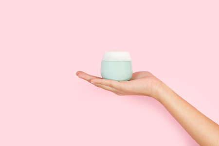 Woman hand holding a moisturizer cream on a pink background with copy space