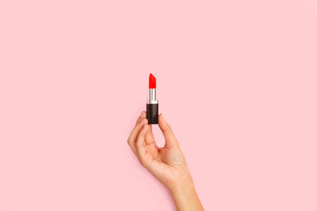 Woman hand holding a red lipstick on a pink background with copy spaceの写真素材