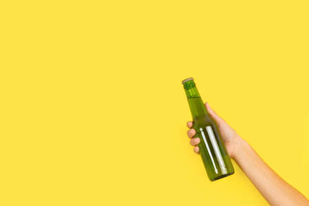 Woman hand holding a green bottle of beer on a yellow background with copy spaceの写真素材