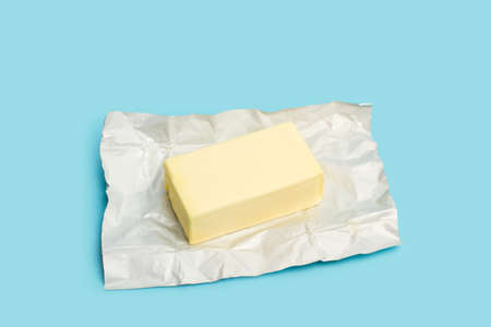 A block of butter on an aluminum paper on a light blue backgroundの写真素材