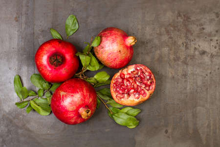 Pomegranates with branches and leaves on a rustic metal table in a top viewの写真素材