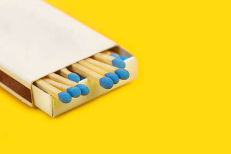 Wooden matches sticks with blue head in a match box on a yellow backgroud and copy space