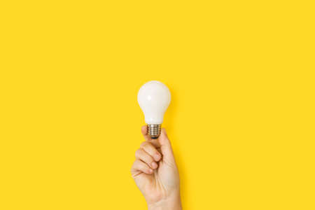 Woman hand holding a light bulb on a yellow background with copy space