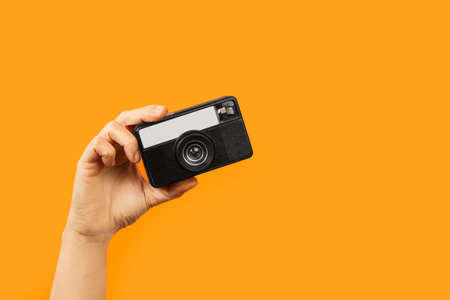 Woman hand holding a vintage camera on an orange backgroundの写真素材