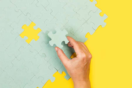 Woman hand holding a pink puzzle piece on a yellow background in a top viewの写真素材