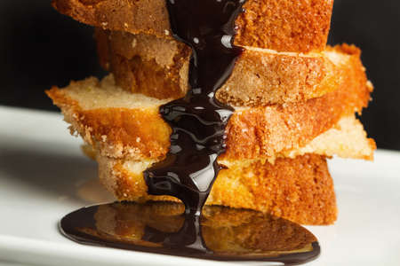 Chocolate sauce on vanilla cake slices on a white plate in a close up view