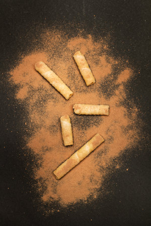 Pieces of wafer rolls with cocoa powder on a dark background in a top view