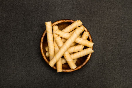 Wafer rolls in a wooden bowl and on a dark background